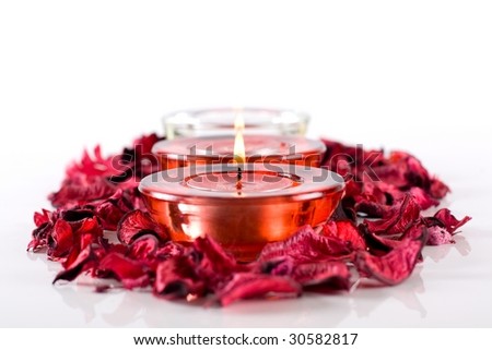 Two red and one white burning candles surrounded with dry, aromatic rose petals