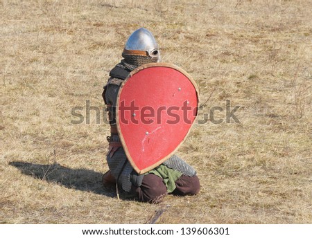 person dressed in an armor of the medieval knight with the weapon and a board in hands