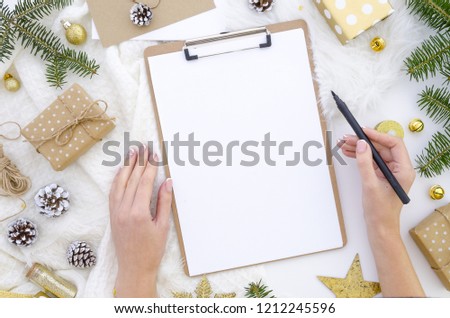 Flat lay christmas clipboard mockup. Woman\'s hands holds black brush pen. Blank white paper sheet clip board mock up. Winter holidays mood for hand lettering. Merry christmas happy new year. Flatlay