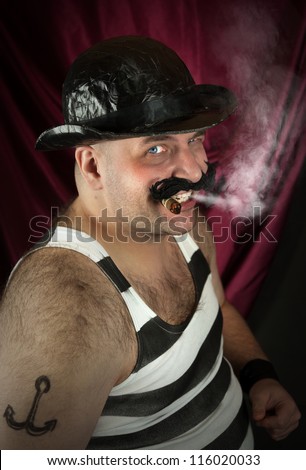 Old fashon circus scene. Young men in circus costume as vintage strongman with bowler hat and smoking cigar