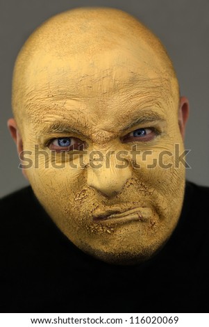Painted face of young man. Yellow cracked paint on grumpy face