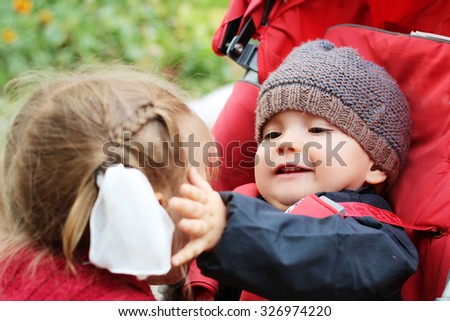 Happy baby looking with love and touching a cheek of his elder sister, outdoor portrait