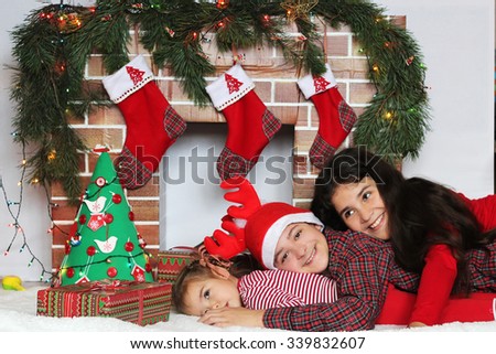 Three smiling children lying near Christmas decorated fireplace, winter holiday family concept