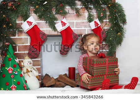 Pretty child girl holding some packed gifts near Christmas decorated fireplace, winter holiday family concept