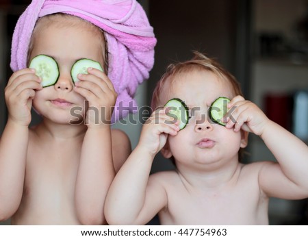 Funny small girl with a bath towel on her head and her small brother holding a piece of cucumber on their eyes like a mask, beauty and health concept, indoor closeup portrait