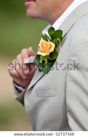 A close-up of the groom on this wedding day showing a yellow rose pinned to his suite
