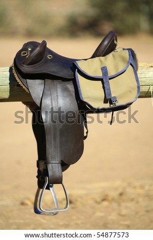 A vertical close up of horse riding gear, including a saddle and bag, in full sunlight