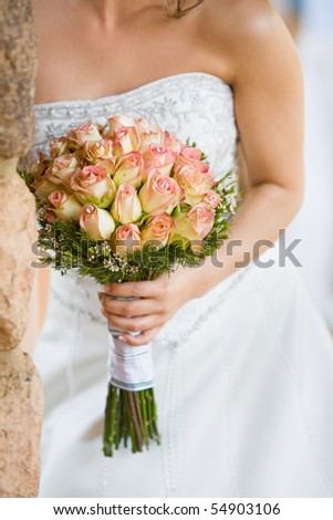 A vertical close up of a caucasian bride holding a bouquet of pink and yellow roses