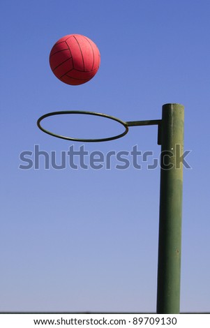 A photo of a red netball falling through a green hoop, with blue sky background
