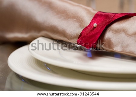 A bronze napkin tied with a maroon ribbon for a wedding's table setting