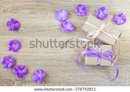 Two gift boxes, purple flowers on wood background with empty space for text. Top view with copy space