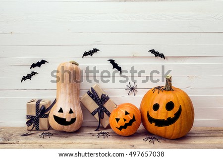 Three pumpkins with painted faces,  gift boxes and decorative spiders on a wooden table on a background of white boards. Background for Halloween. Space for text.