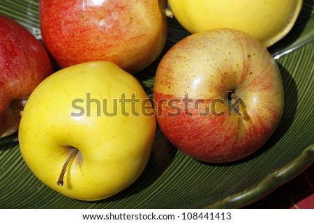 Yellow and red apples on green plate, focus on one each yellow & red in foreground.
