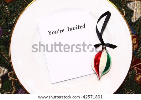 White paper with the words YOU\'RE INVITED printed on it and vintage Xmas ornament on top of round white plate.