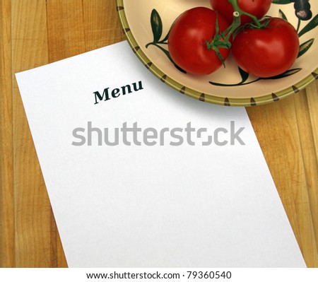 White paper with word  MENU and copy space on cutting board with decorative Italian bowl of red tomatoes on the vine.