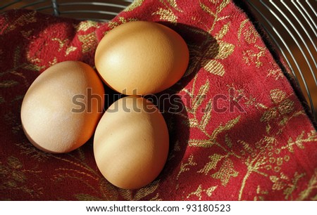 Fresh brown eggs on decorative red towel in the morning sun.
