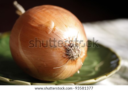 Whole yellow onion with roots and skin resting on green plate.