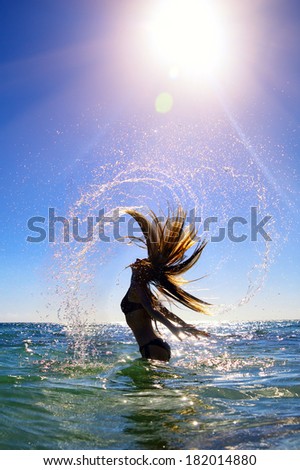 Beautiful young woman with long hair splashing water in sea
