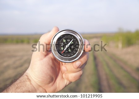 hand holding a compass in front of a choice between two paths in the wood