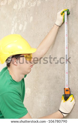 The builder measures the length of the tape measure on the background of a concrete wall