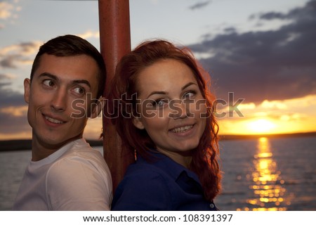 Young couple sitting on summer beach based on a column enjoying sunset?
