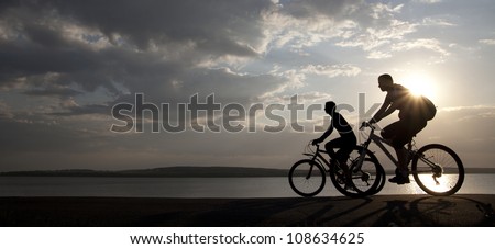 Image of sporty couple on bicycles outdoors against sunset. Silhouette.