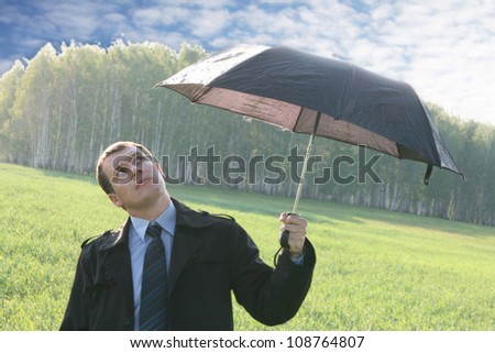 Businessman finding protection outside in the field  Businessman with umbrella in the umbrella peeps out from under - predicts future weather - forecast gives