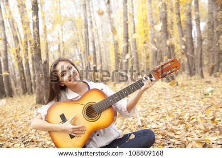Young latin girl in autumn forest with guitar sunder the falling leave selective focus