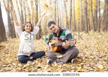 couple enjoying themselves in autumn forest with a guitar the guy playing the acoustic guitar and the girl throws up on a dry yellow poplar leaves