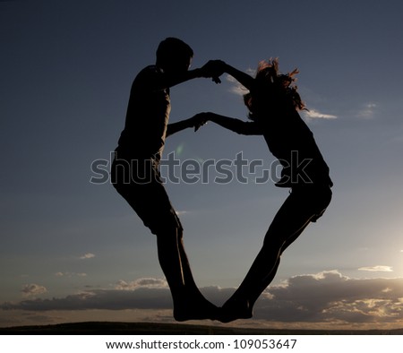 boy and girl jumping up holding hands against sunset sky with clouds - the symbol of victory success and achieving