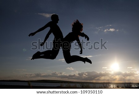 Silhouettes of couple jumping on sunset background