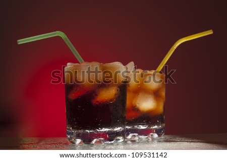 two glasses of cola lemonade with ice and tubes on red background Space for inscriptions