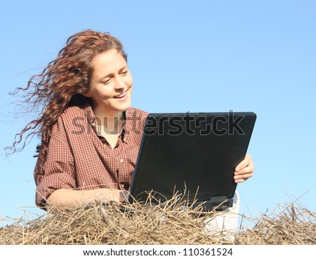 Country ginger girl typing on laptop lying on haystack