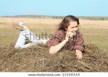 Attractive woman in blue jeans and shirt lies  in hay and with blue sky in background (copy space)