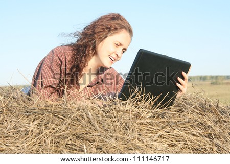 Country ginger girl typing on laptop lying on haystack
