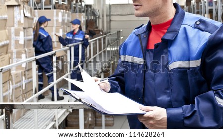 warehouse three workers- one man and two woman in a special blue uniform is recording and accounting of contents in cardboard boxes in stock No faces idea account statistics rediscount cargo arrival