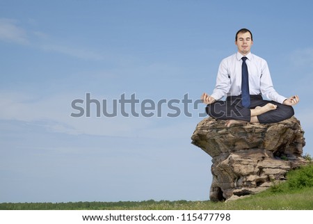 Businessman meditating on a rock in the mountains