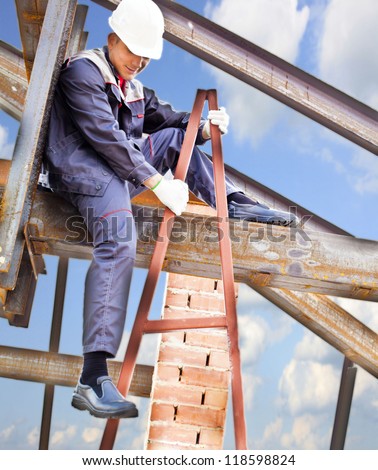 worker on a steel beam raises his hands sitting on the metal structure metal beam - roof frame, Under construction on blue sky background