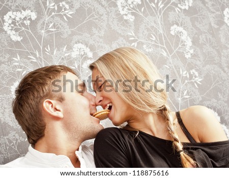young couple sitting on a couch together a cookie bite her lips