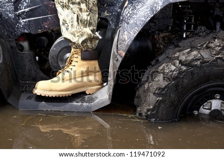 hand in yellow leather boot standing on the steps of the ATV standing in a muddy puddle