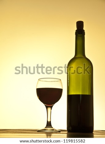 Elegant red wine glass and a wine bottle in yellow gradient background