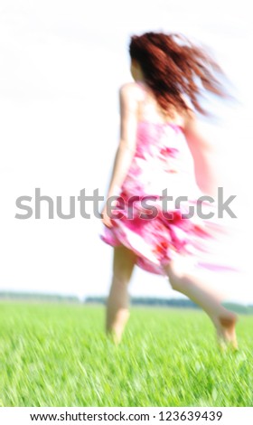 Blurred Back view young woman in red dress running over green grass No focus