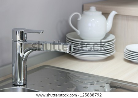 steel kitchen sink with a stack of plates and porcelain teapot