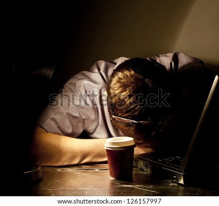 man in evening light, table lamp sleeping at his desk in front of a black laptop