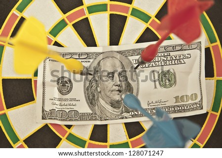 Bulls eye with dollar bill pinned by 3 darts, close up