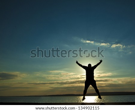 black silhouette of man in happy jump on orange sunset sky and sea