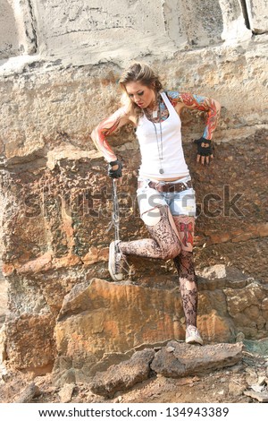 woman painted body art in the form of fire in the t-shirt and denim shorts and torn pantyhose on the background of the industrial buildings of reinforced concrete slabs