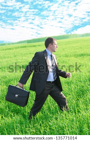 Businessman walks with suitcase in the green grass  field go to future ahead