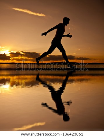young runner with water reflecting   Silhouette of man running at sunset.