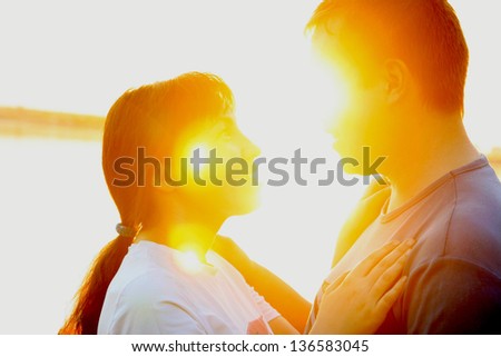 Young couple silhouette hugging and looking at each other outdoors at sunset background
